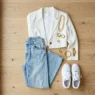 Overhead view of aesthetic outfit with vintage wide-leg jeans, cropped white blazer and chunky gold jewelry on wood floor