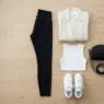 Complete sporty chic outfit arranged on wood floor showing cream blazer, black leggings, white crop top, sneakers and accessories
