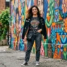Woman wearing concert outfit with jeans and band tee posed against colorful street mural in natural daylight