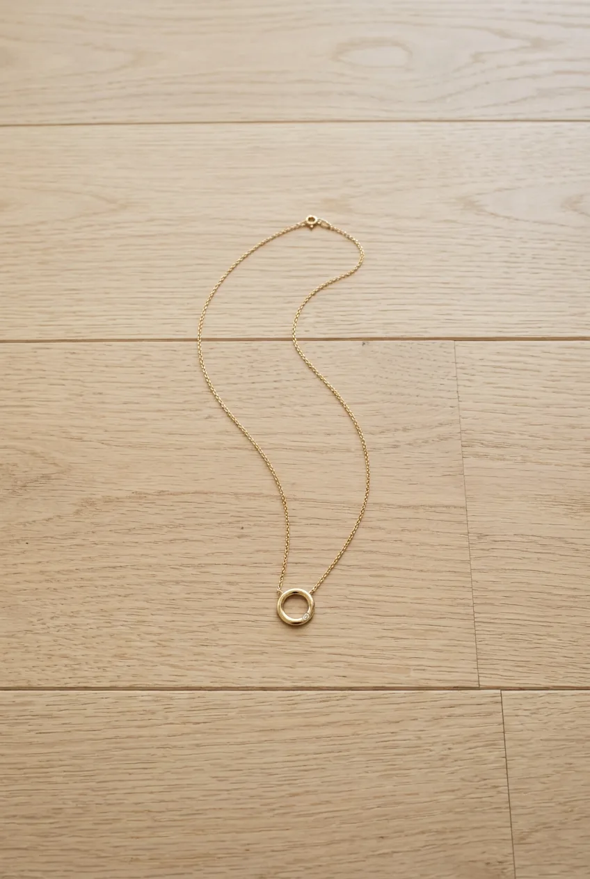 Delicate gold chain necklace with simple pendant arranged minimally on light wood floor