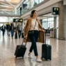 Woman walking through modern airport terminal with carry-on luggage wearing comfortable travel outfit