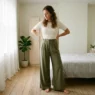 Woman wearing wide-leg trousers and fitted top showing full silhouette in softly lit bedroom