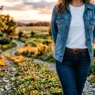 Woman wearing unbuttoned medium wash denim jacket over white t-shirt in golden hour lighting