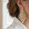 Elegant gold and pearl chandelier earrings hanging from woman's ear with white blouse collar