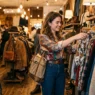 Woman browsing through Japanese vintage clothing rack in warmly lit boutique with golden lighting