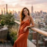 Woman in elegant outfit standing on rooftop terrace during golden hour with city skyline