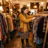 Woman browsing clothing racks in warmly lit vintage boutique with styled outfit visible