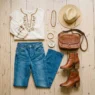 Complete boho chic outfit flat lay with peasant blouse, flared jeans, ankle boots and accessories on wood floor