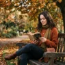 Woman on a park bench reading a book in a cozy autumn sweater outfit, soft dappled light through trees