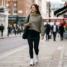 Woman in olive hoodie and black leggings walking on a city sidewalk in soft morning light