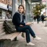 Woman in casual school outfit sitting on bench with backpack in urban setting