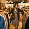 Woman flipping through clothing racks in warmly lit vintage boutique with styled outfit visible