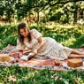 Woman reclining on picnic blanket wearing flowing summer outfit in dappled golden sunlight