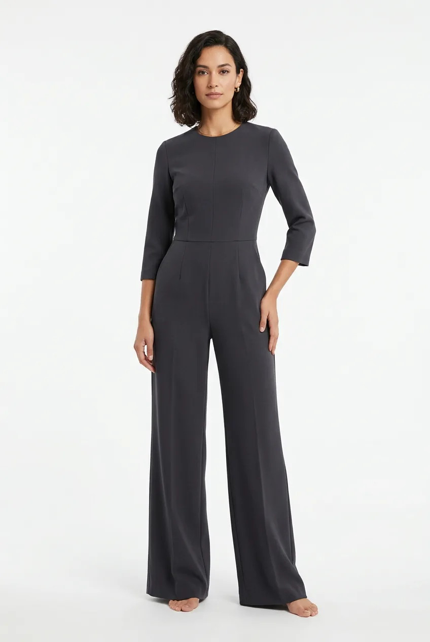 Woman wearing sharply tailored wide-leg charcoal crepe jumpsuit with structured bodice, studio setting