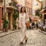 Woman in tailored monochrome cream trouser suit walking along a warm European cobblestone street in late afternoon sunlight