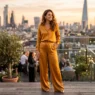 Woman wearing a liquid amber-gold wide-leg satin co-ord on a rooftop terrace at golden hour with city skyline behind her