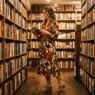 Woman in a warmly lit bookstore wearing a bold floral midi dress with block-heeled mules and a leather belt