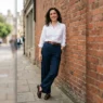 Woman in crisp white Oxford shirt tucked into wide-leg navy trousers with loafers against red brick wall